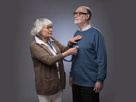 Old couple. Senior woman taking care, checking heart beat of husband with stethoscope