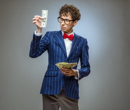 Happy smiling man in a suit holding fan of dollar banknotes on gray background