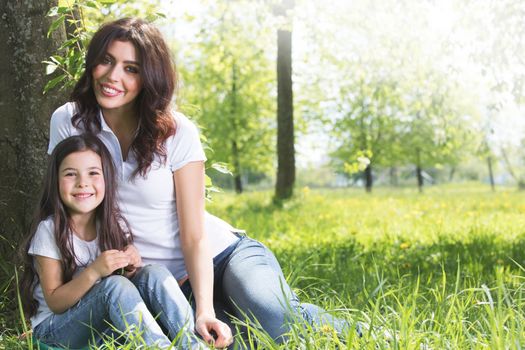 Beautiful young mother and daughter relaxing sitting on grass in park