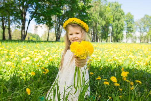 Sweet little girl with floral head wreath on and flowers bunch in hands in summer park