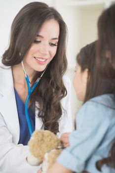 Beautiful female pediatrician doctor examining child with teddy bear in office