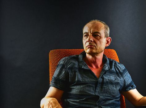 Creative portrai. Middle aged man sitting in an armchair. Portrait of mature man on black background