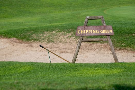 Chipping green sign in front of bunker on golf course, detail of golf ground