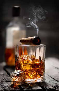 Cigar and glass with whiskey with ice cubes