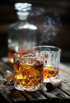Cigar and glass with whiskey with ice cubes