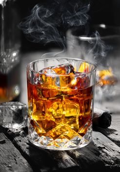 Cigar and glass with whiskey with ice cubes