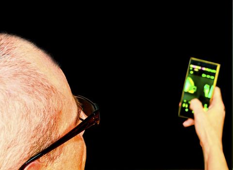 Middle aged man with glasses sitting in an armchair. Mature man with mobile phone on black background. Copy space. Senior concept. 