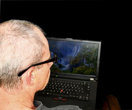 Middle aged man with glasses sitting in an armchair. Mature man using notebook on black background. Copy space. Senior concept. 