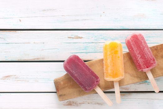 Various flavored ice popsicles over wooden background