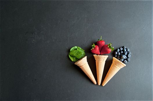 Natural ingredients spilling out of an icecream cones including strawberry, mint and blueberry flavors