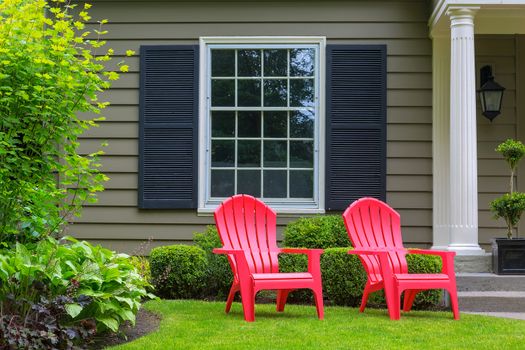 Red outdoor chairs on green grass lawn of house manicured front yard