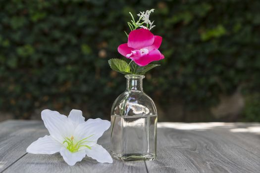 a bottle and some flowers on a wooden table outdoors in the summer