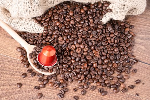 Coffee capsule on wooden spoon and  roasted coffee beans with burlap sack on wooden background.top view.