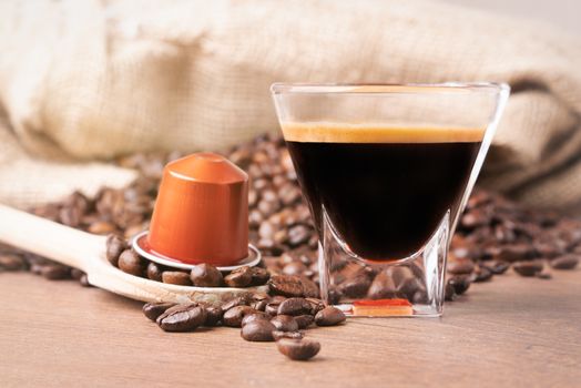 Cup of coffee with coffee capsule on wooden spoon, roasted coffee beans on wooden background,front view.