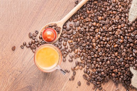 Cup of coffee with coffee capsule on wooden spoon, roasted coffee beans on wooden background,top view.