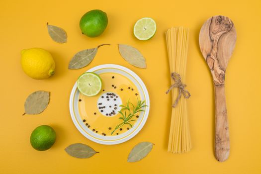 Cooking ingredients on bright yellow background. Limes, lemons, laurel leaves, pasta and spices.