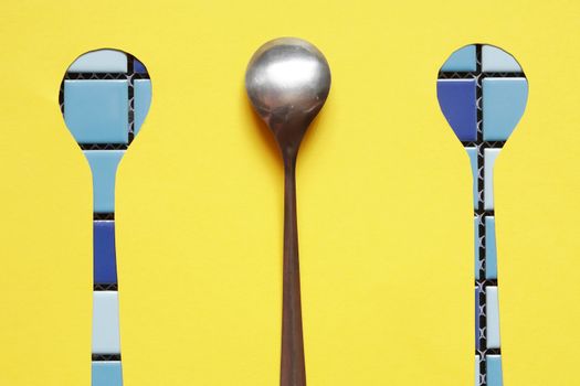 Abstract concept. One metal spoon with two spoons gap against yellow paper