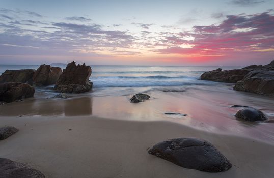 Beautiful colours of the sunrise  and waves flow onto the beach and around rocks.  Location:  Zenith Beach, Port Stephens Australia