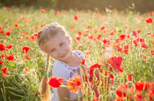 Young girl with bouquet among poppies field at sunset