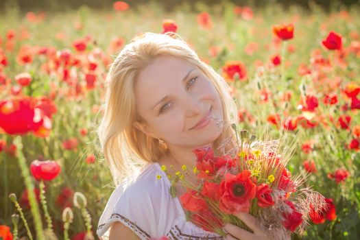 Woman with bouquet among poppies field at sunset