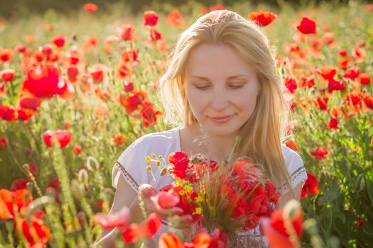 Woman with bouquet among poppies field at sunset with hands up