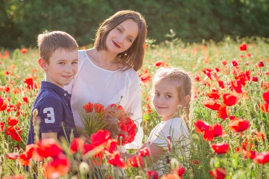 Mother in white with son and daughter holding bouquet on blossoming red poppies field