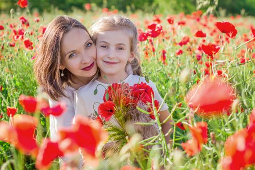 Mother brunette in a white dress with daughter together on blossoming red poppies field