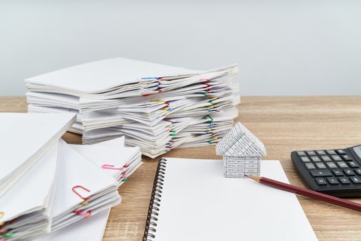 House and pencil on notebook with calculator have overload paperwork report of sale and receipt on wooden table with white background and copy space. Business and finance concept success.