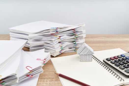 House on notebook with calculator have blur pencil and overload paperwork report of sale and receipt on wooden table with white background and copy space. Business and finance concept success.