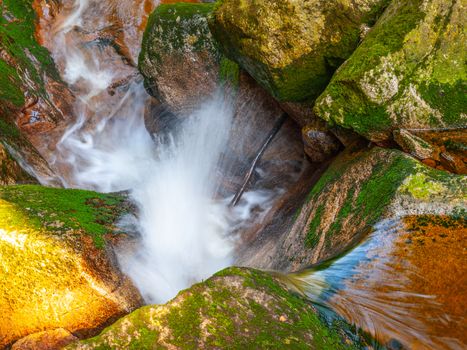 Water cascade of small creek between mossy stones. Long exposure