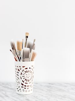 Paintbrushes in a white decorative vase, on marble surface.