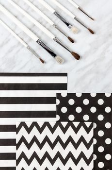 Paint brushes and decorative paper for arts and crafts, on marble background.