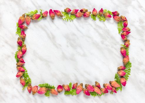 Frame made of dried roses and green leaves, on marble background.