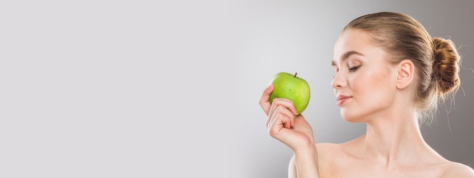 Beautiful young nude woman with green apple close up on gray background with copy space
