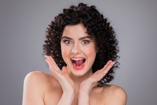 Surprised excited beautiful woman screaming amazed in joy, gray background