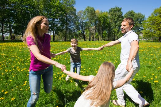 Happy family of parents and children dancing in park holding hands