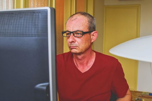 Middle aged man with glasses sitting at desk. Mature man using personal computer. Senior concept. Man working at home office