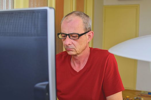 Middle aged man with glasses sitting at desk. Mature man using personal computer. Senior concept. Man working at home office