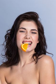 Young funny woman biting slice of orange, healthy eating concept