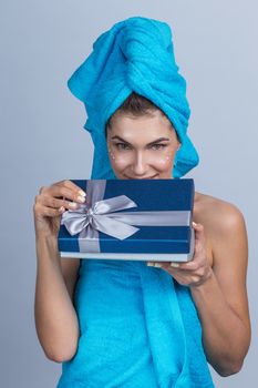 Beautiful woman with towel on head applying creme after shower and holding gift box