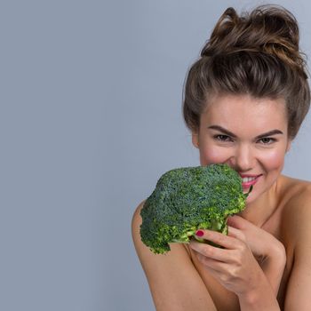 Portrait of a beautiful woman with perfect skin holding broccoli, gray background