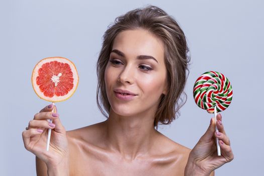 Young woman holding slice of grapefruit and lollipop candy, healthy eating concept