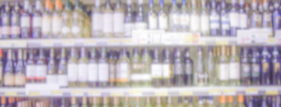 Defocused background with shelves of wine bottles in a supermarket or hypermarket convenience store. Intentionally blurred post production for bokeh effect