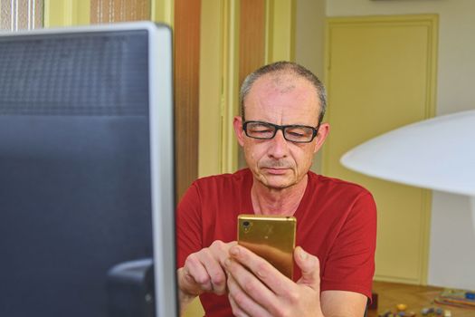 Middle aged man with glasses sitting at desk. Mature man using mobile phone. Senior concept. Man at home office