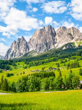 Rocky ridge of Pomagagnon Mountain above Cortina d'Ampezzo with green meadows and blue sky with white summer clouds, Dolomites,, Italy.