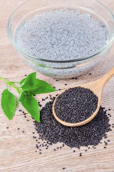 Lemon basil seeds in wooden spoon and soak in water with green leaf on wooden background.