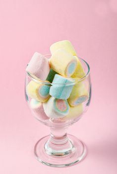 Colorful mini marshmallows in modern glass on pink background.