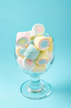 Colorful mini marshmallows in modern glass on blue background.