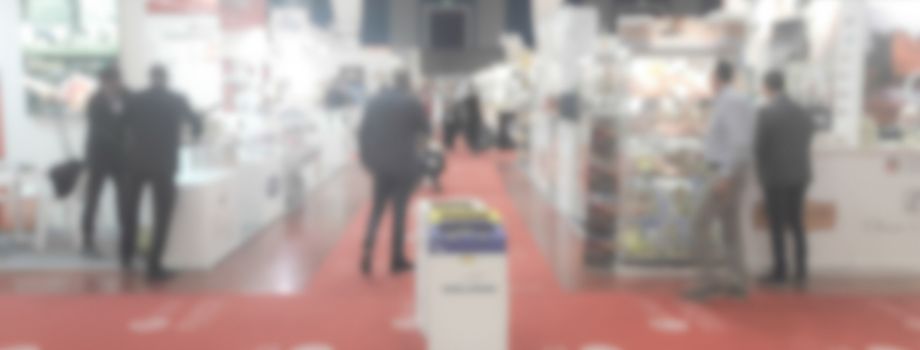 Defocused background of a trade show with people visiting the commercial exhibition. Intentionally blurred post production for bokeh effect