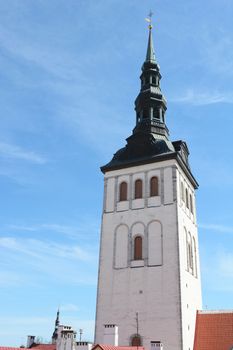 St Nicholas Church in Tallinn, Estonia. The white tower is topped by a black spire, against a blue sky.